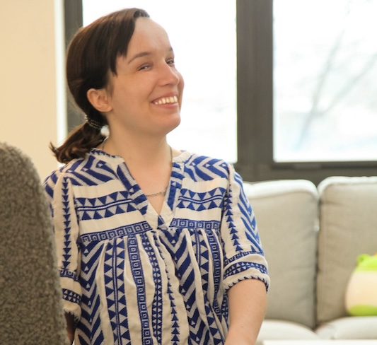 A smiling resident sits in a chair in her apartment.