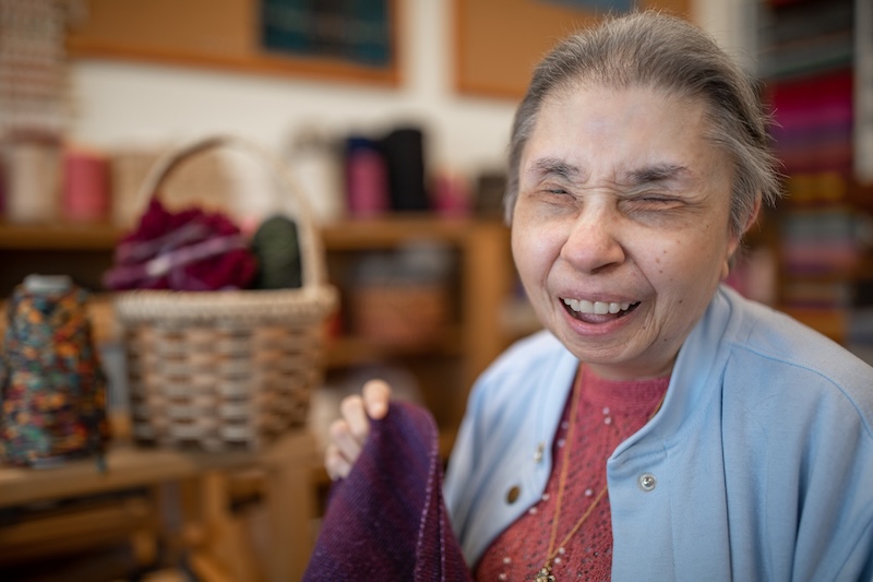 A smiling resident sits surrounded by yarn in our therapeutic weaving room.