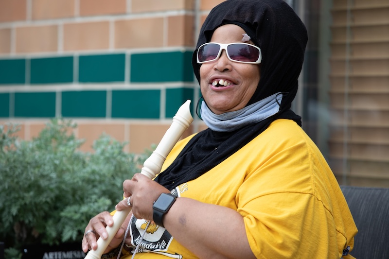 A smiling resident sits our outdoor courtyard while holding a recorder instrument.
